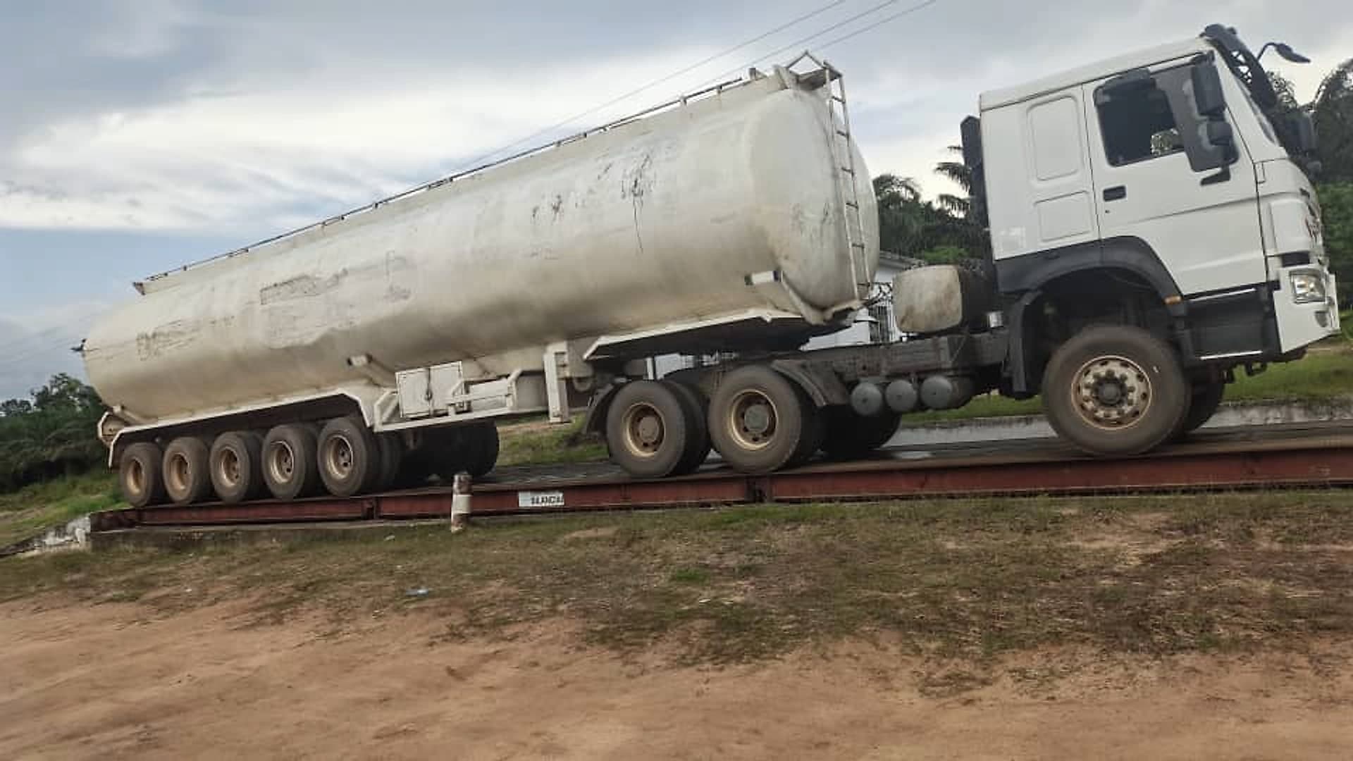 An articulated tanker on the weighbridge platform beside the plantation